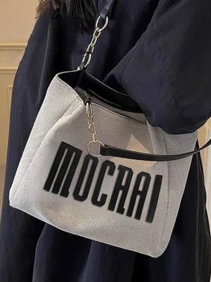 Textured canvas shoulder bag in light grey with black chain accents and bold lettering.
