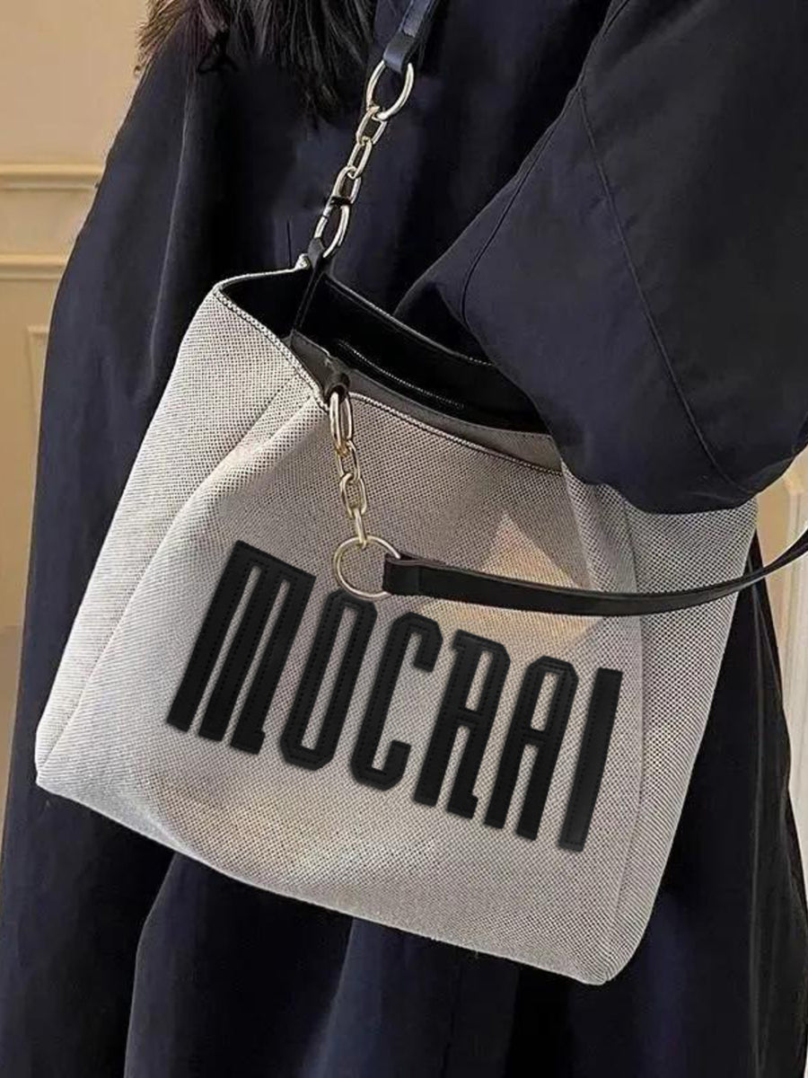 Textured canvas shoulder bag in light grey with black chain accents and bold lettering.