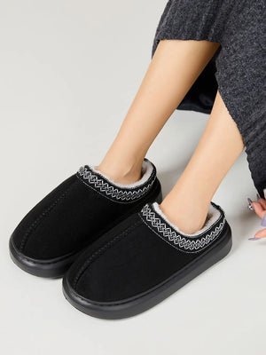 Black shearling house slippers with embroidered trim and cozy lining.