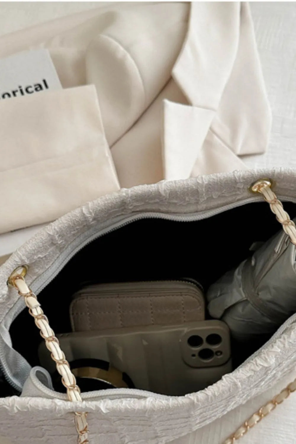White bouclé shoulder bag with chain strap, showing interior contents: phone, wallet, and umbrella.