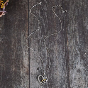 Silver heart necklace with crystal accents and gold "MOM" cutout, on a delicate chain.
