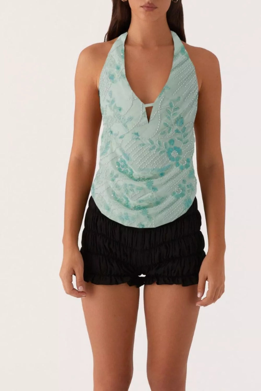 Halter top in mint green with floral embroidery and beaded details, paired with black ruffled shorts.