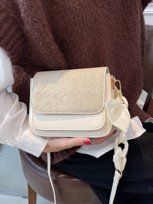 Mini crossbody bag in beige with embossed cartoon pattern and ribbon detail