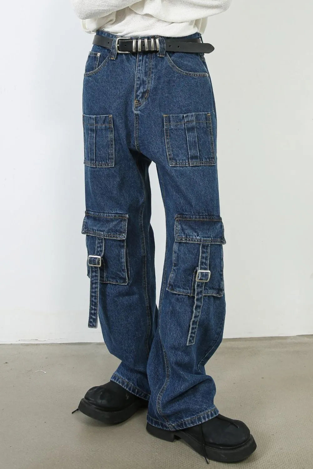 Medium wash denim cargo pants with buckle strap pockets and wide legs.