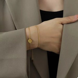 Gold double layered titanium steel bracelet with circular charm and delicate chain.