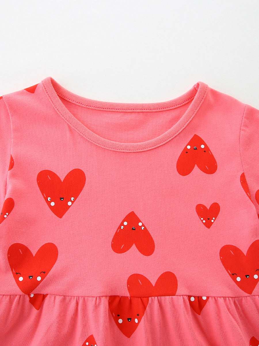Pink cotton baby dress with red heart print and ruffled hem.