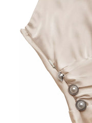 Champagne satin maxi dress with V-neck, spaghetti straps, and pearl button detail.