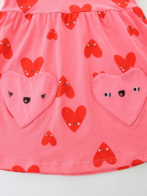 Pink cotton baby dress with red heart print and two heart-shaped pockets with embroidered faces.