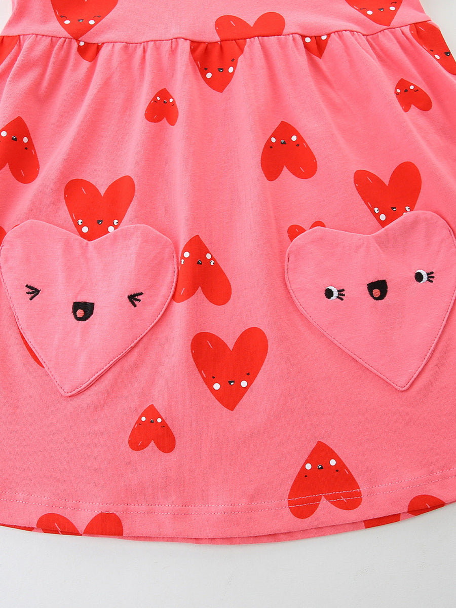 Pink cotton baby dress with red heart print and two heart-shaped pockets with embroidered faces.
