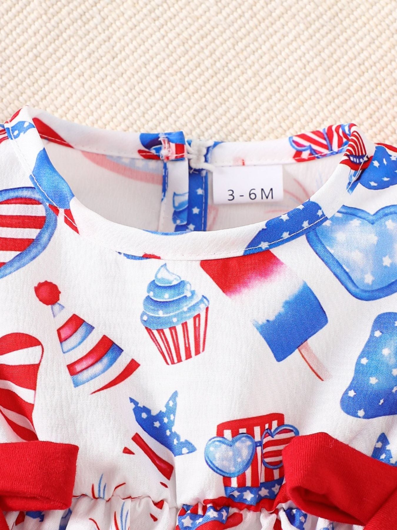 Baby one-piece with patriotic print, cupcakes, popsicles, and hearts. Ruffle sleeves and red bows.