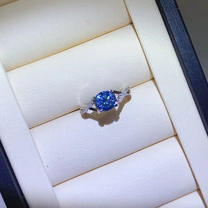 Silver twisted pavé moissanite engagement ring with a blue center stone.