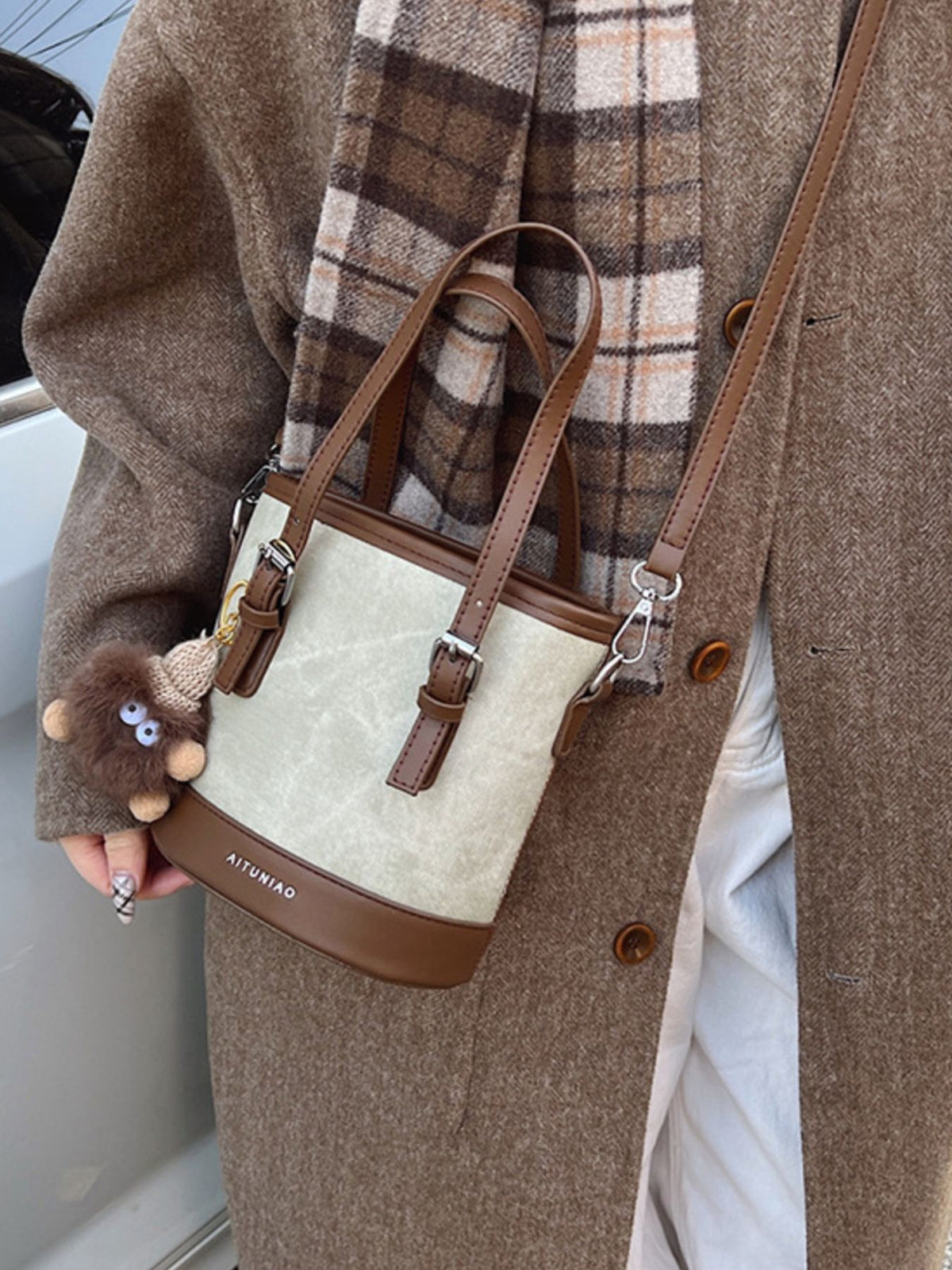 Premium two-tone bucket crossbody bag in cream with brown trim and strap, featuring a fuzzy charm.