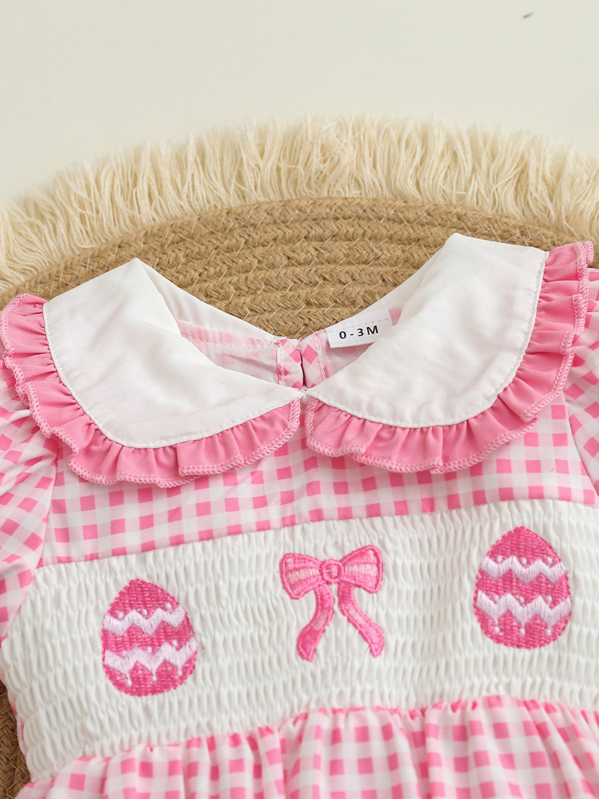 Pink gingham one-piece with smocked chest, embroidered Easter eggs and bow, white ruffled collar.