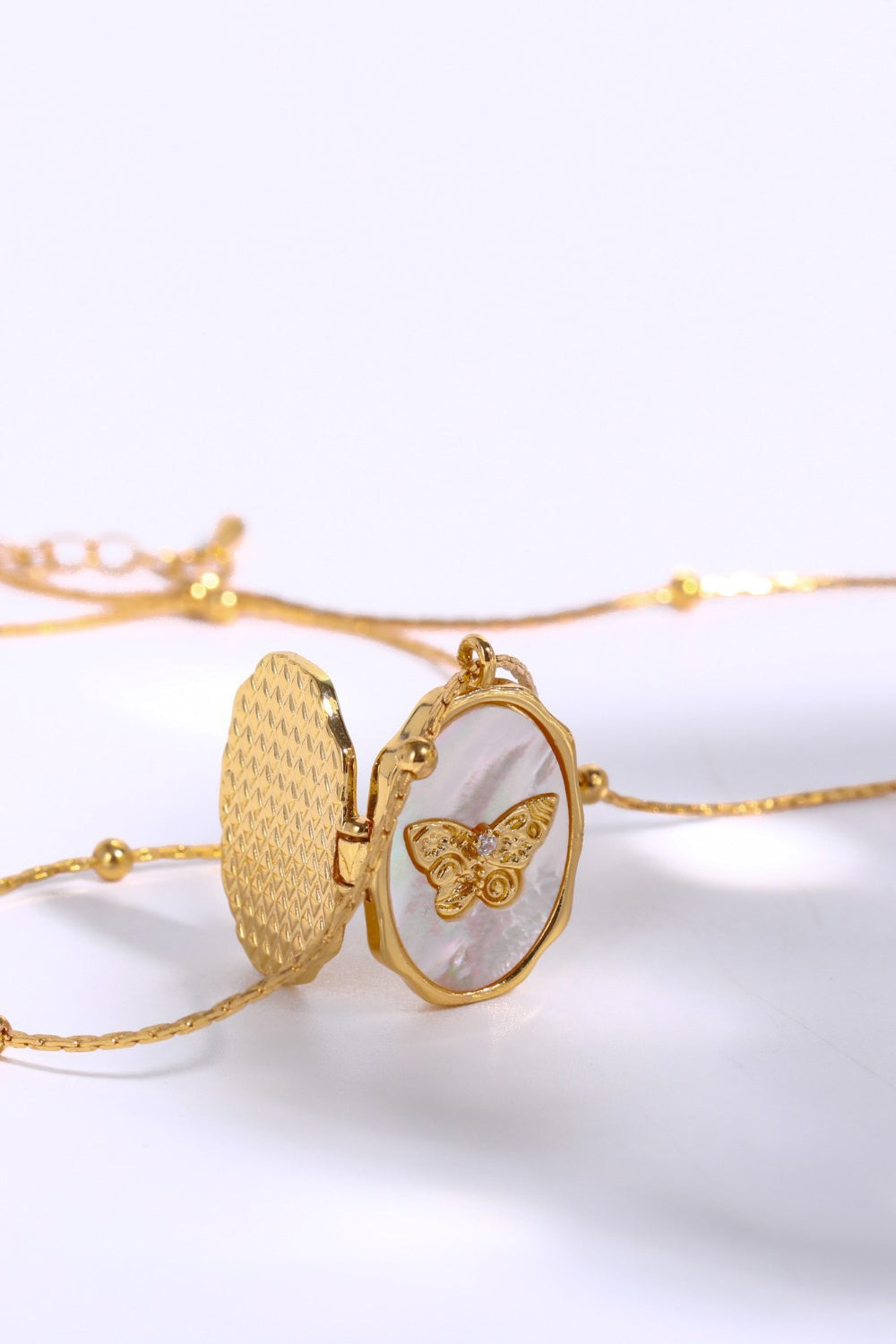 Gold locket necklace with open butterfly charm on mother of pearl, delicate beaded chain