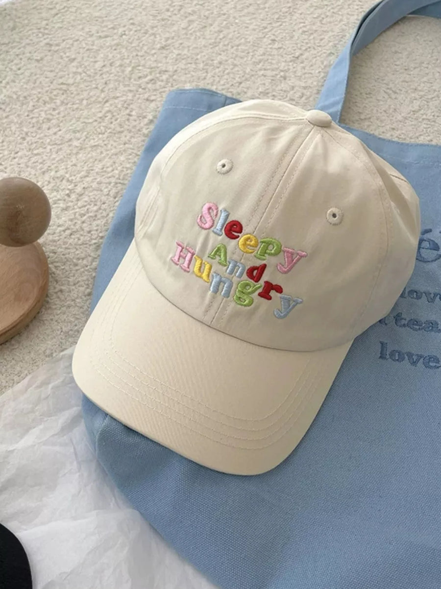 Beige baseball cap with "Sleepy And Hungry" embroidered in colorful letters.