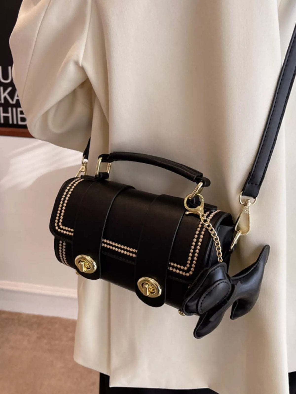 Mini black PU leather crossbody bag with gold hardware and dog charm accessory.