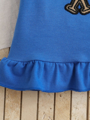 Blue cotton tee with ruffled hem and baseball patch detail.