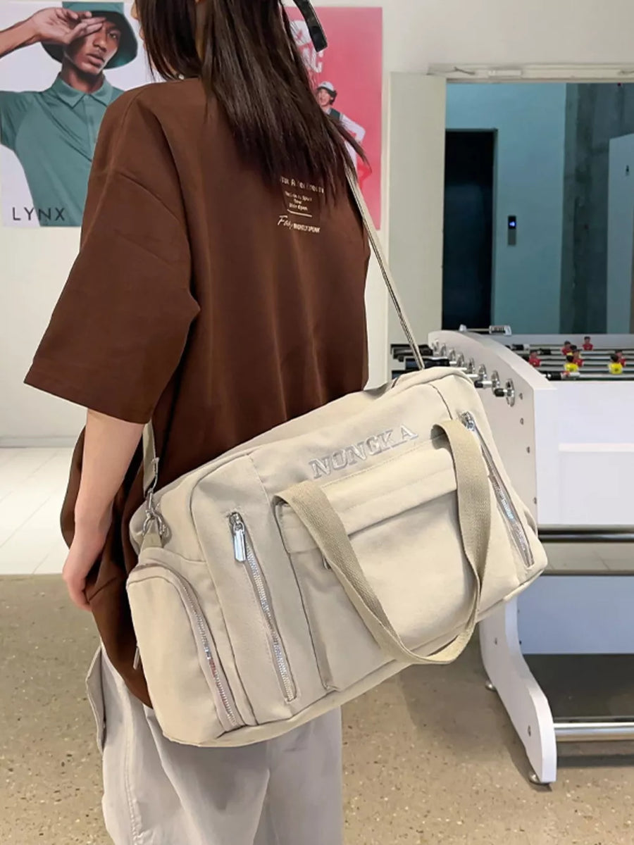 Beige canvas duffel bag with multiple zippered pockets and adjustable crossbody strap.