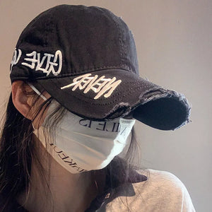 Black distressed denim baseball cap with white embroidery and frayed brim.
