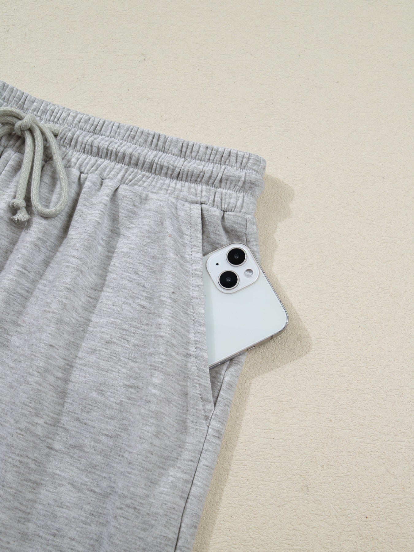 Grey polyester lounge pants with drawstring waist and side pocket holding a phone.