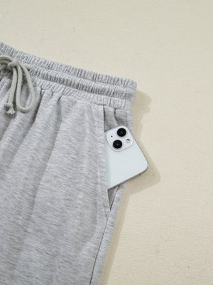 Grey polyester lounge pants with drawstring waist and side pocket holding a phone.