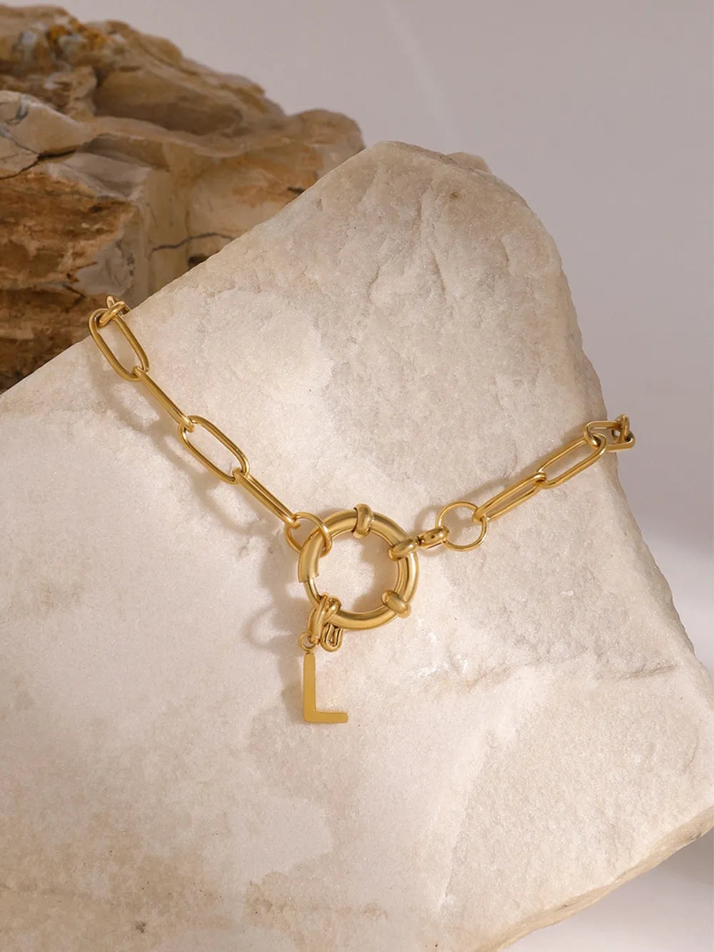 Gold chunky chain bracelet with a circular clasp and an initial L charm.