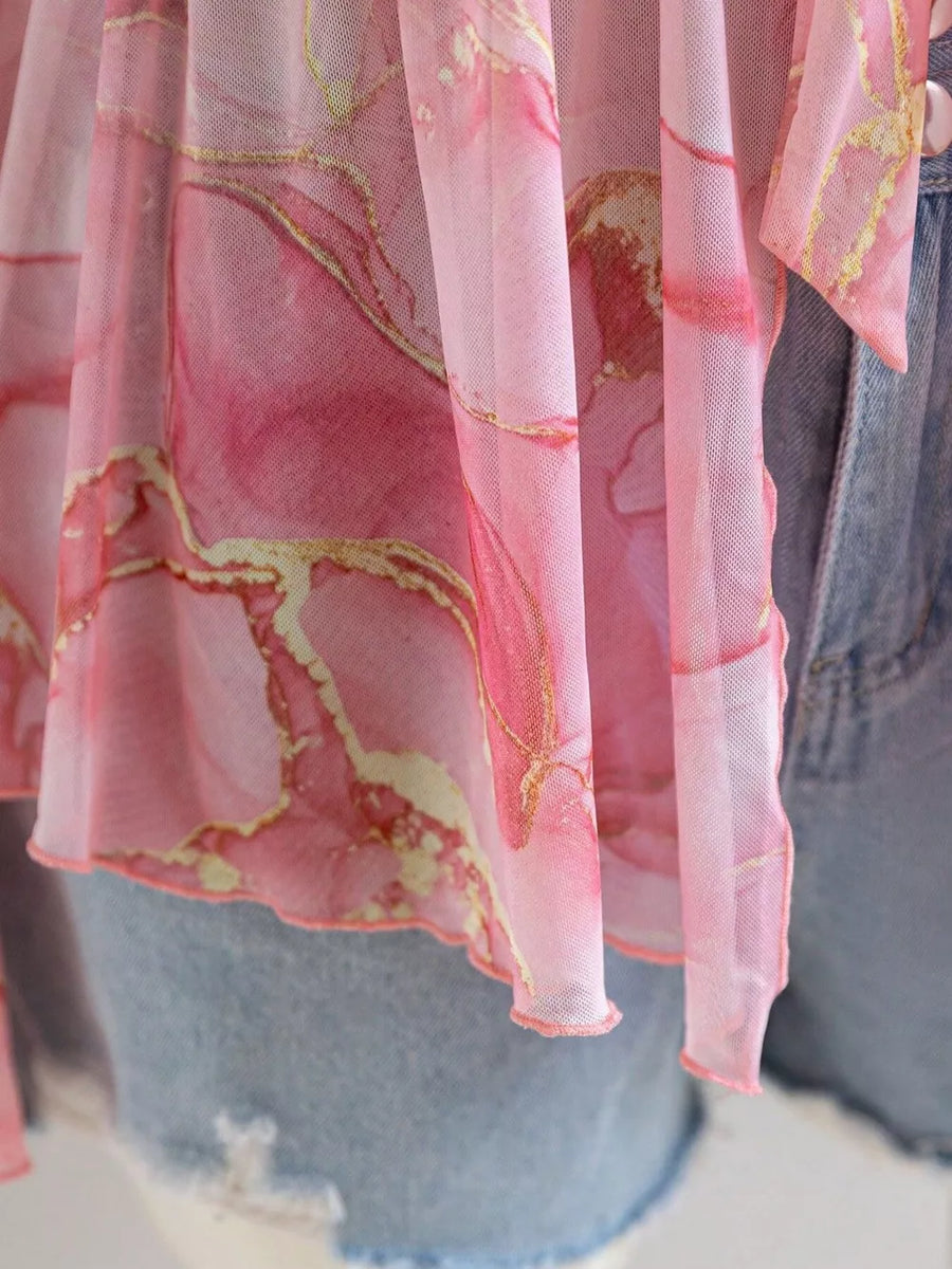Pink chiffon blouse with abstract floral print and gold accents, featuring a tied detail.