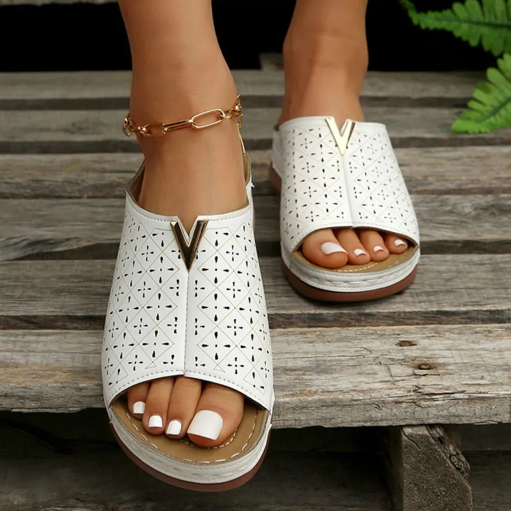 White laser-cut leather platform slides with V-detail and gold ankle chain.