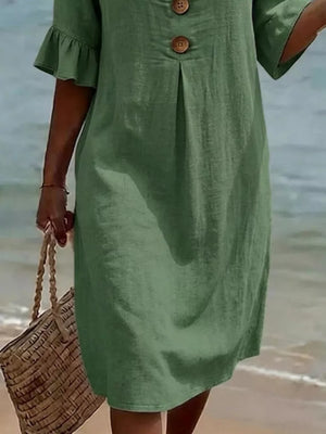 Green linen dress with ruffled sleeves and button detail, styled with a straw bag.