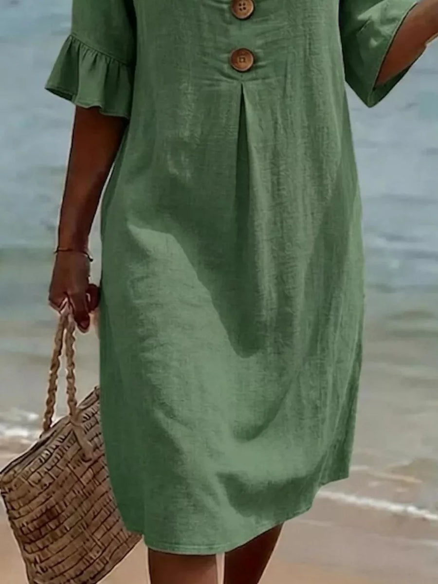 Green linen dress with ruffled sleeves and button detail, styled with a straw bag.