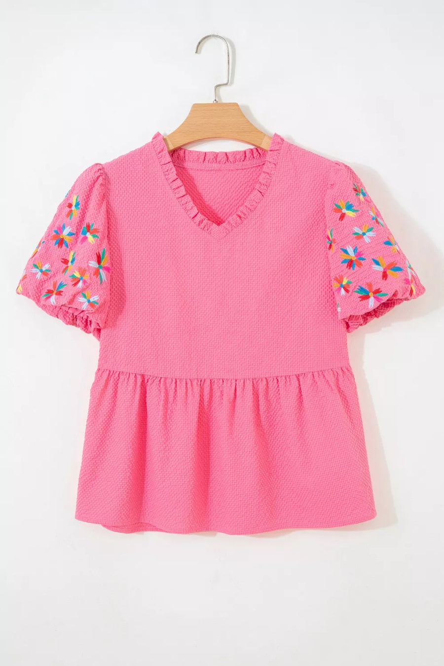 Women's pink textured peplum blouse with embroidered floral puff sleeves and ruffled V-neck.