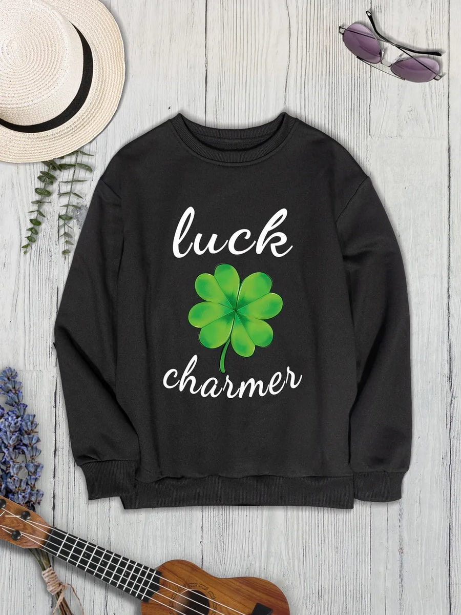 Black graphic sweatshirt with white "luck charmer" text and a green clover graphic.