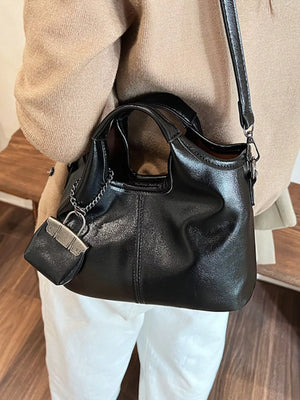 Chic black PU leather crossbody bag with top handles and a decorative mini bag charm.