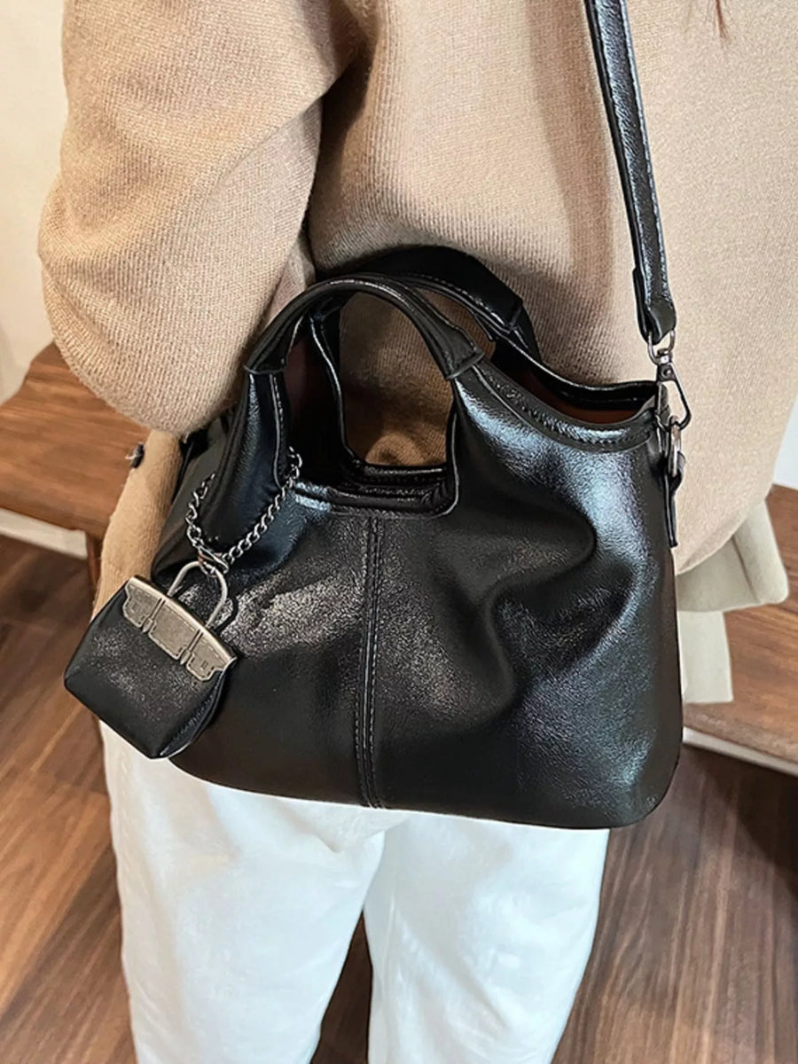 Chic black PU leather crossbody bag with top handles and a decorative mini bag charm.