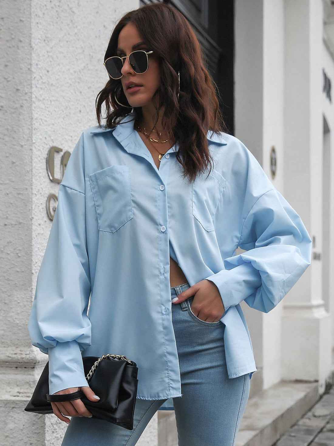 Blue oversized poplin blouse with blouson sleeves and button front, styled with jeans.