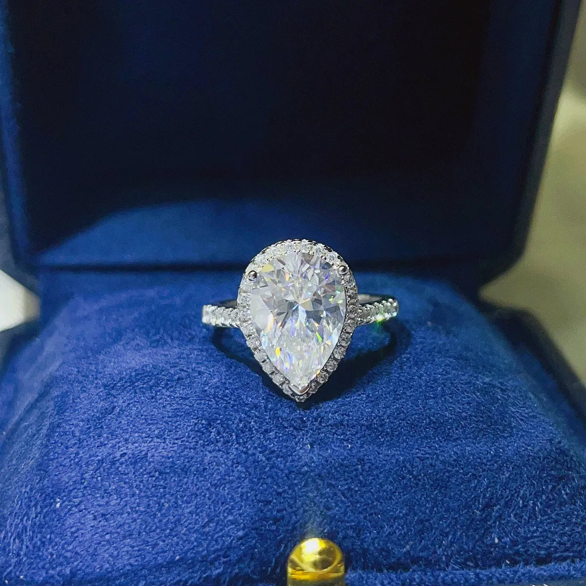 White pear-cut halo engagement ring with pave band in a blue box