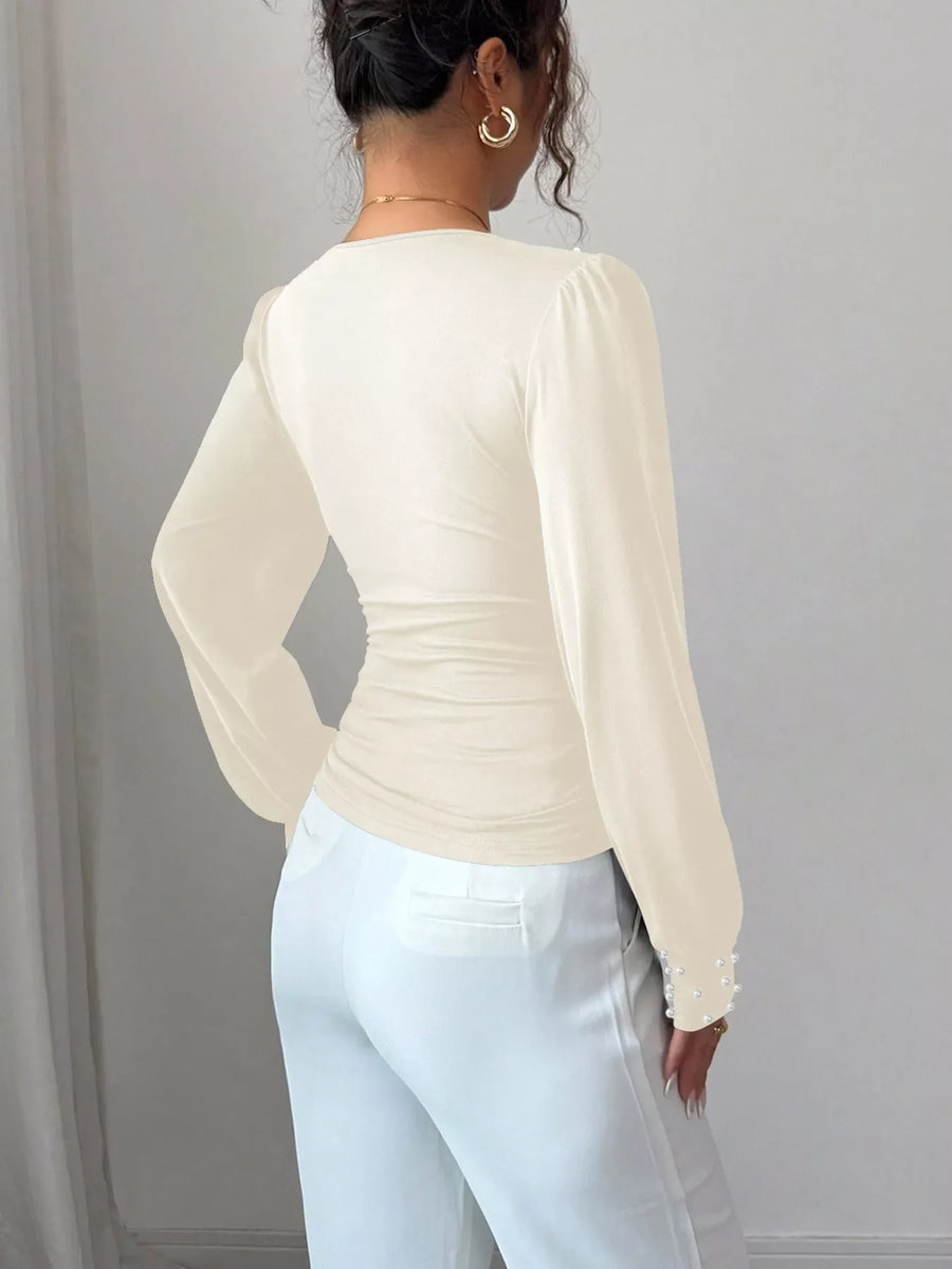 Beige ruched V-neck blouse with pearl embellished cuffs and long sleeves.