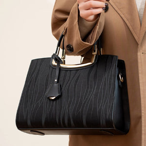 Black embossed tote bag with gold hardware and decorative wave pattern