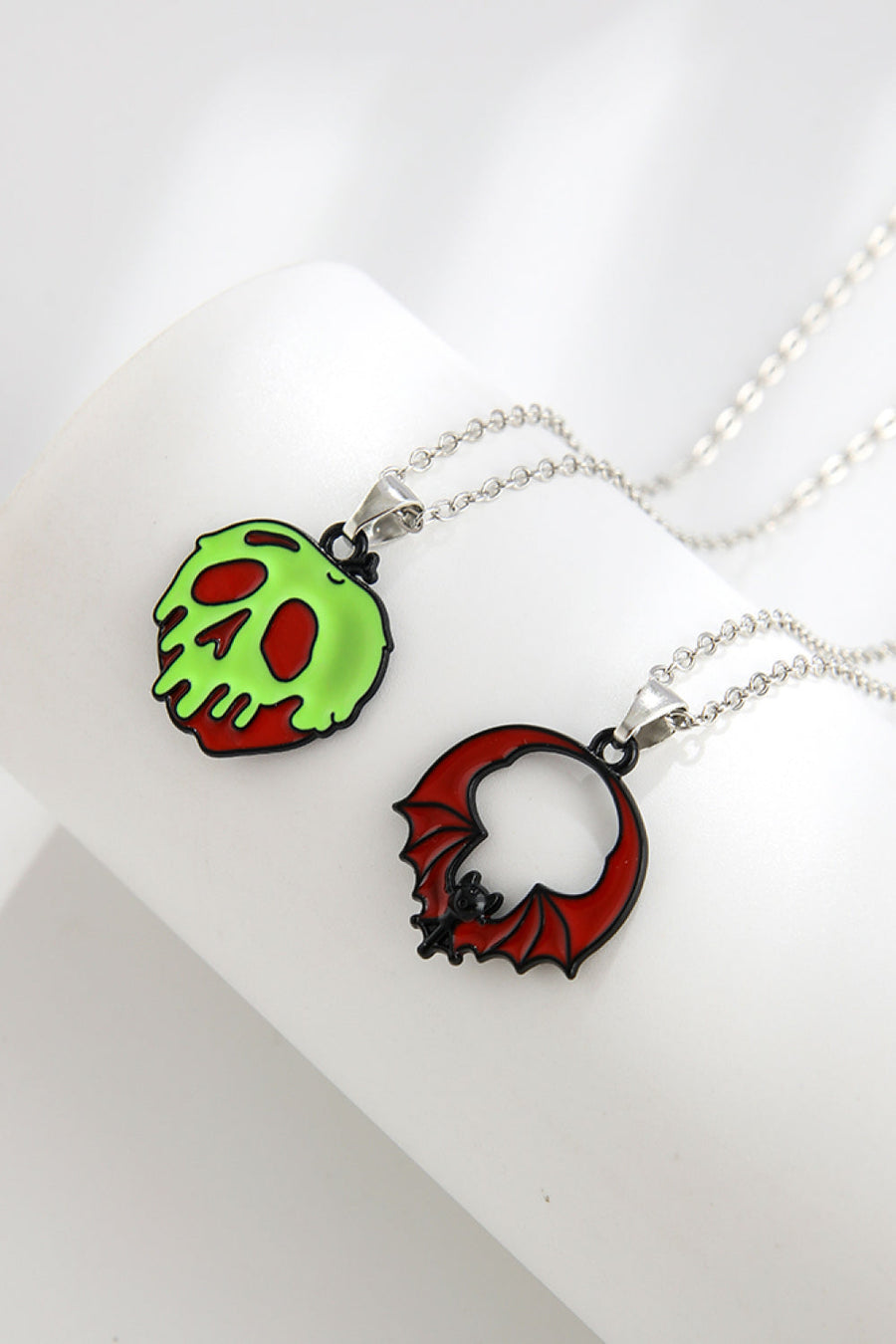 Spooky season enamel pendant necklaces, one green skull, one red bat.