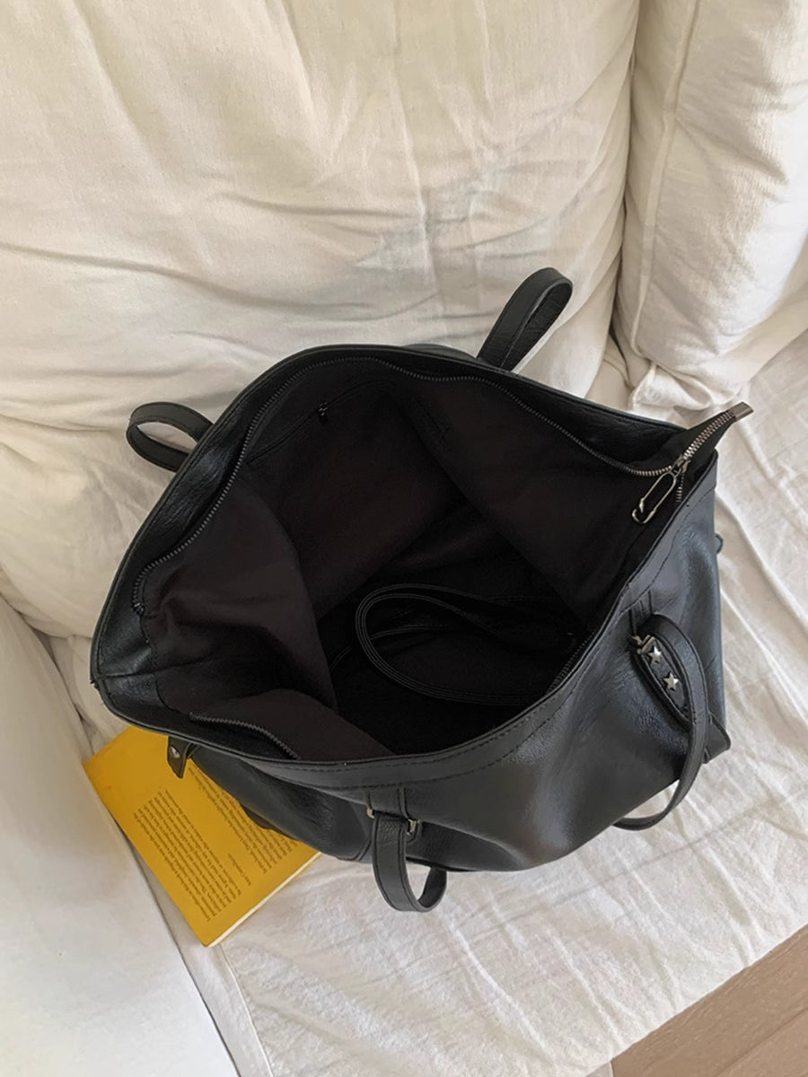 Black faux leather tote bag with star details and zipper closure, open view.
