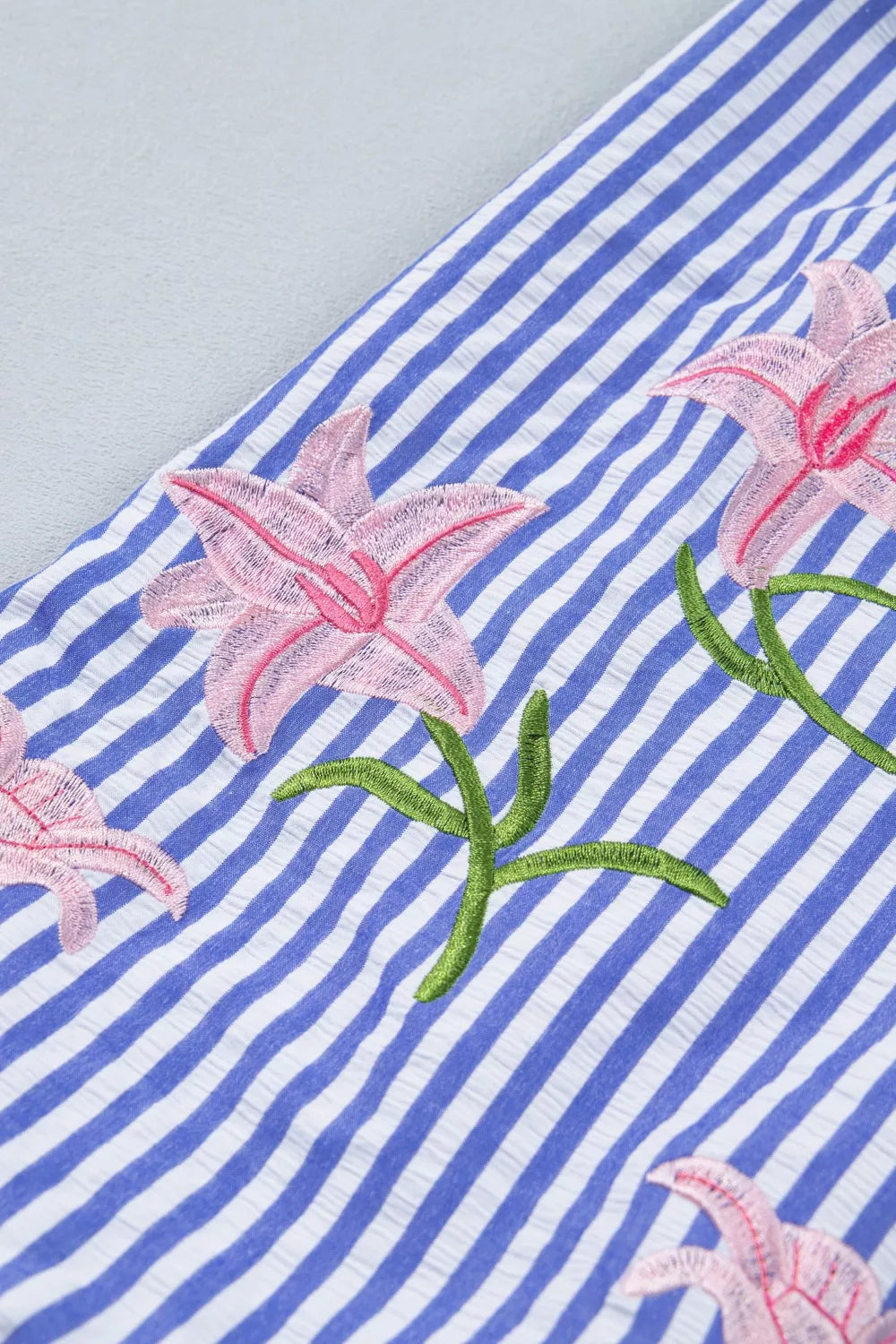 Blue and white striped button-down shirt with pink floral embroidery and green stems.