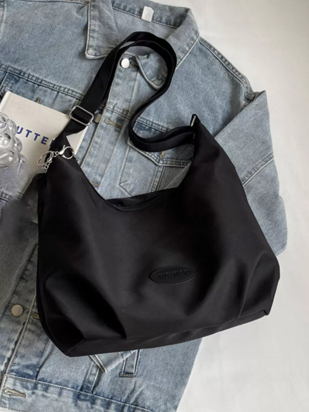 Black canvas shoulder bag with adjustable strap and oval logo detail
