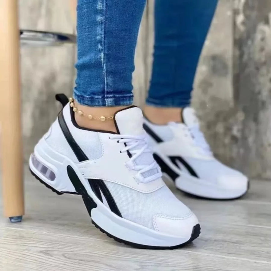 White lace up air cushion sneakers with black accents and a chunky sole.