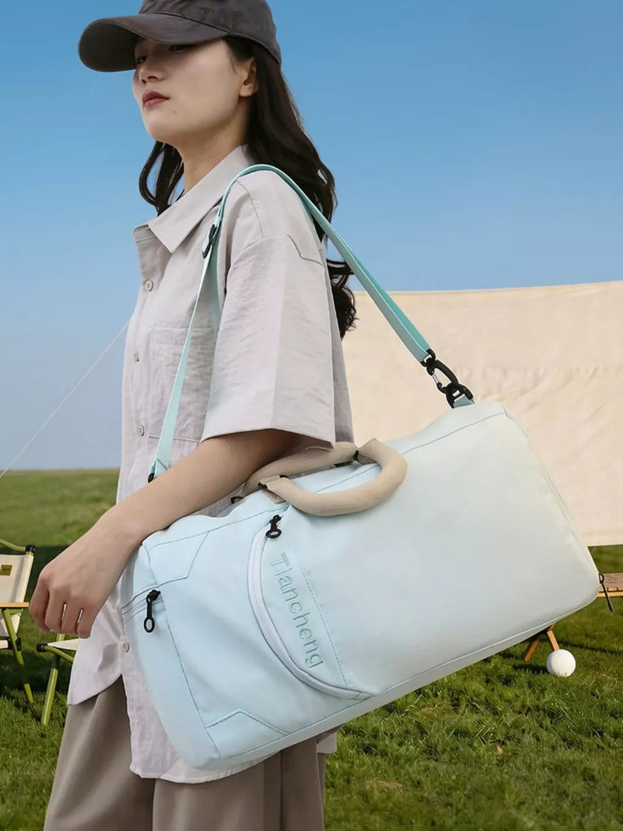 Light blue duffel bag with tan handles and a teal strap, featuring a zippered pocket and embossed text.