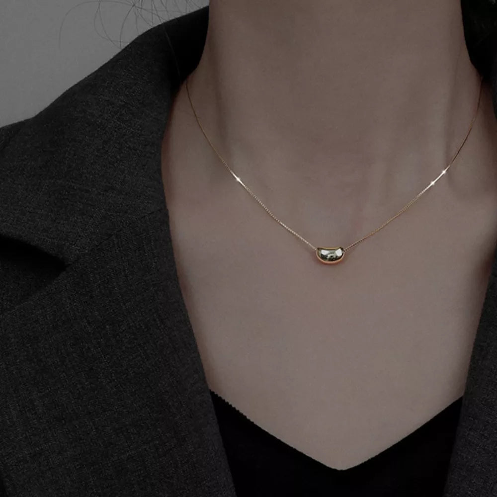 Gold bean pendant necklace on a delicate box chain, styled with a blazer.