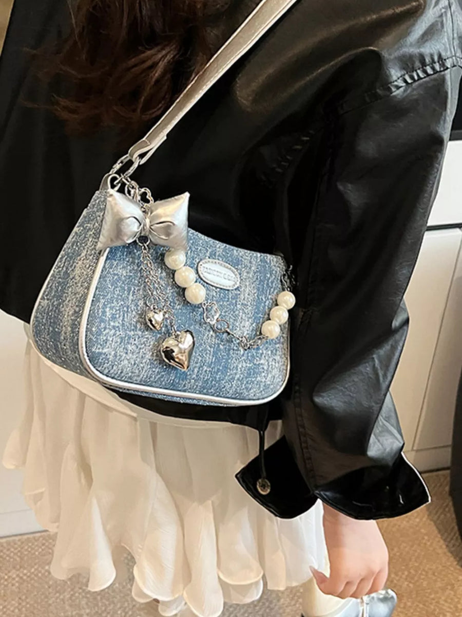 Denim shoulder bag with pearl chain, silver bow, and heart charms.