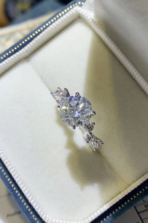 Silver moissanite halo ring with a central round-cut stone and smaller accent stones.