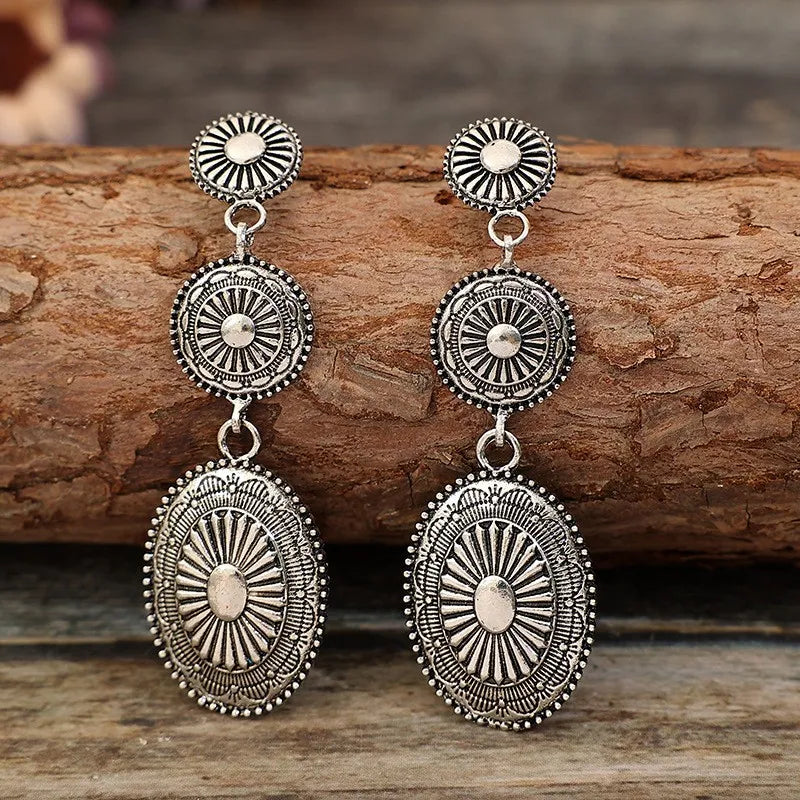Silver sunburst drop earrings with oval and round patterned charms.