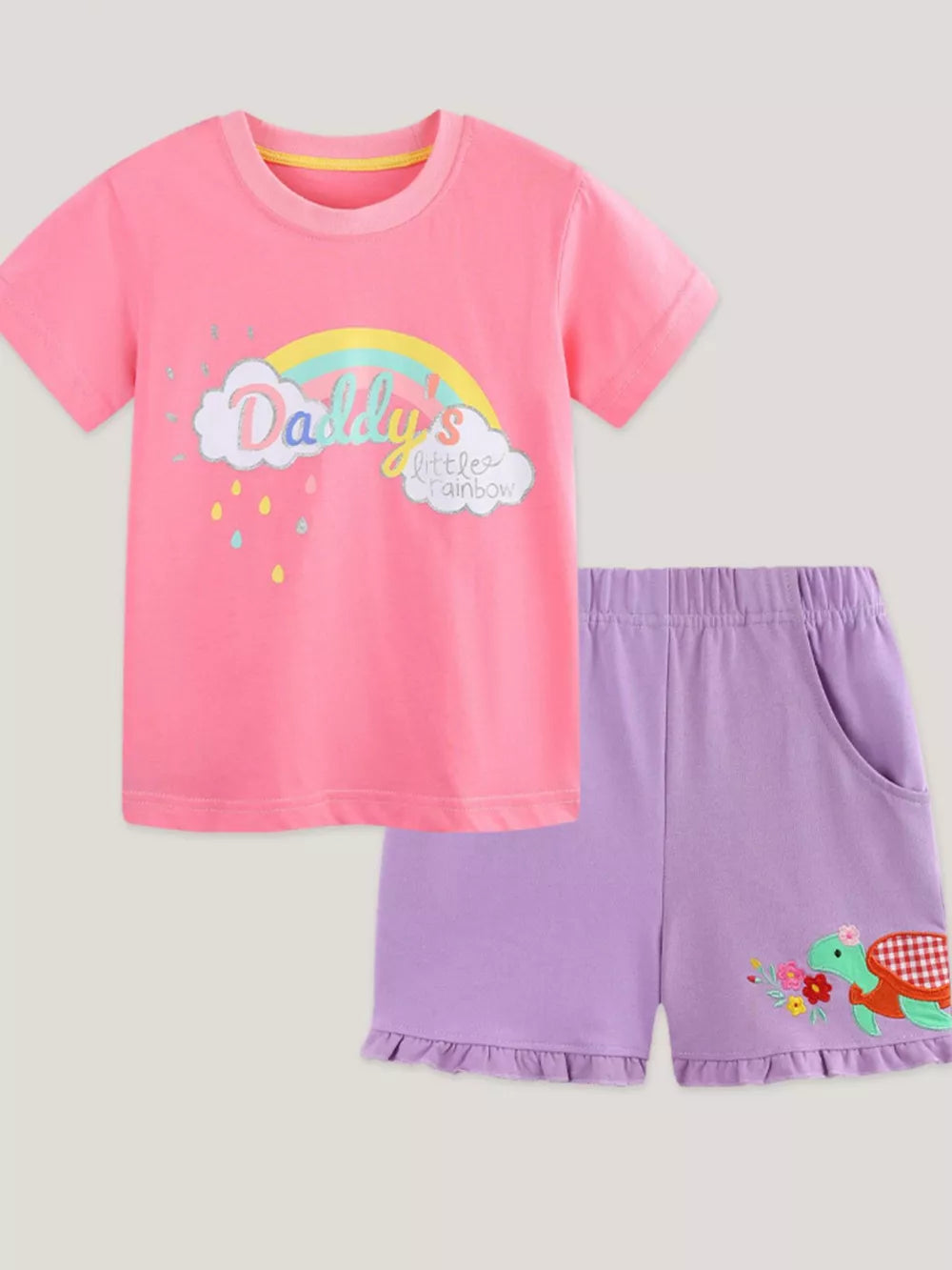 Pink cotton tee with rainbow cloud graphic and purple ruffle shorts with turtle embroidery.