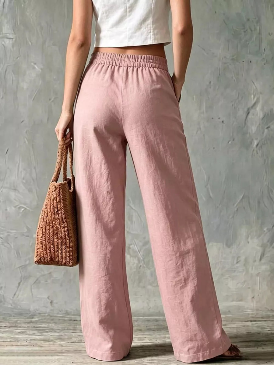 Pink linen wide-leg pants with elastic waistband and pockets, styled with a straw bag.